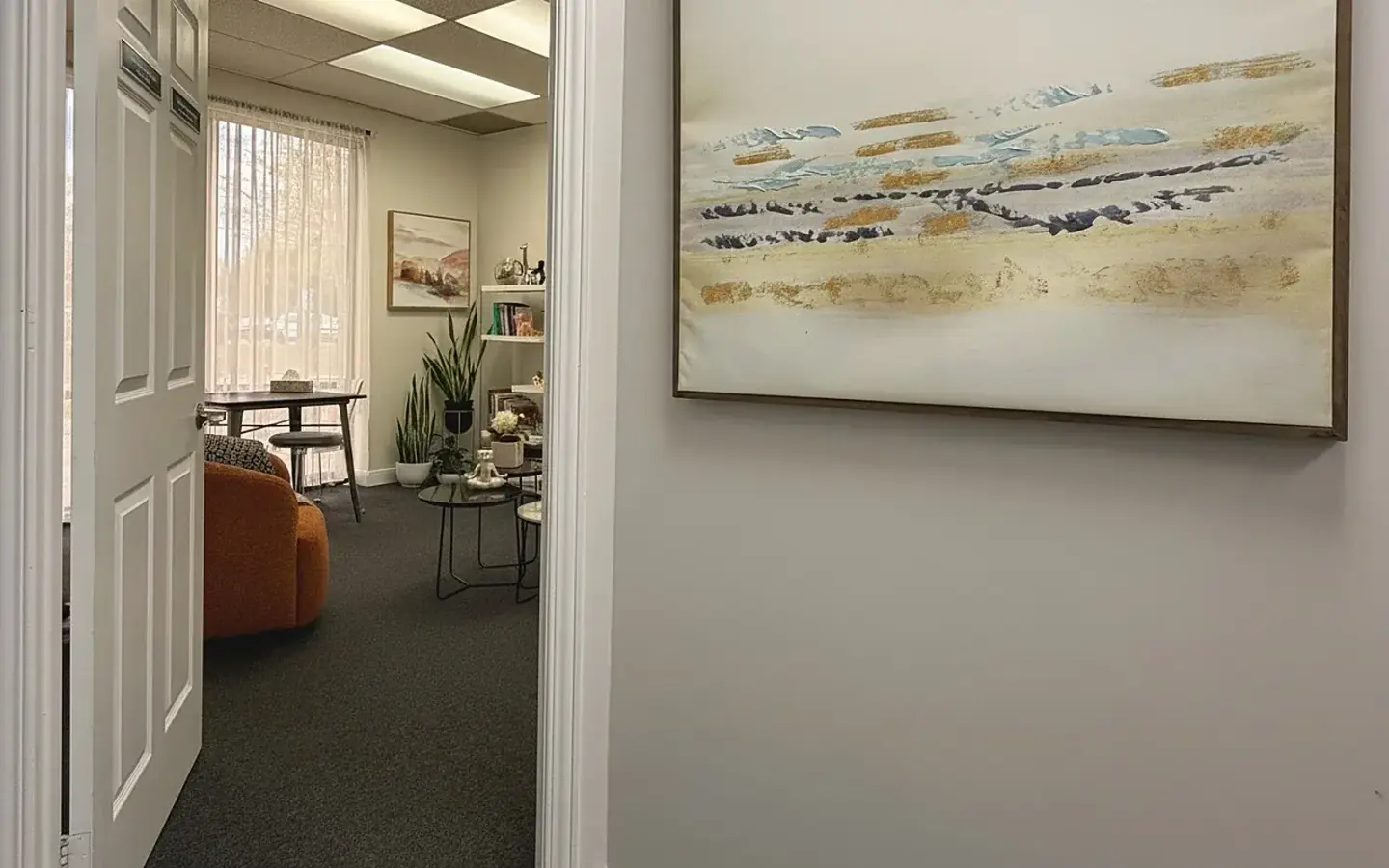 Doorway into the Oakville session room: cream and rust interior visible through the open door, abstract landscape painting in the hallway.